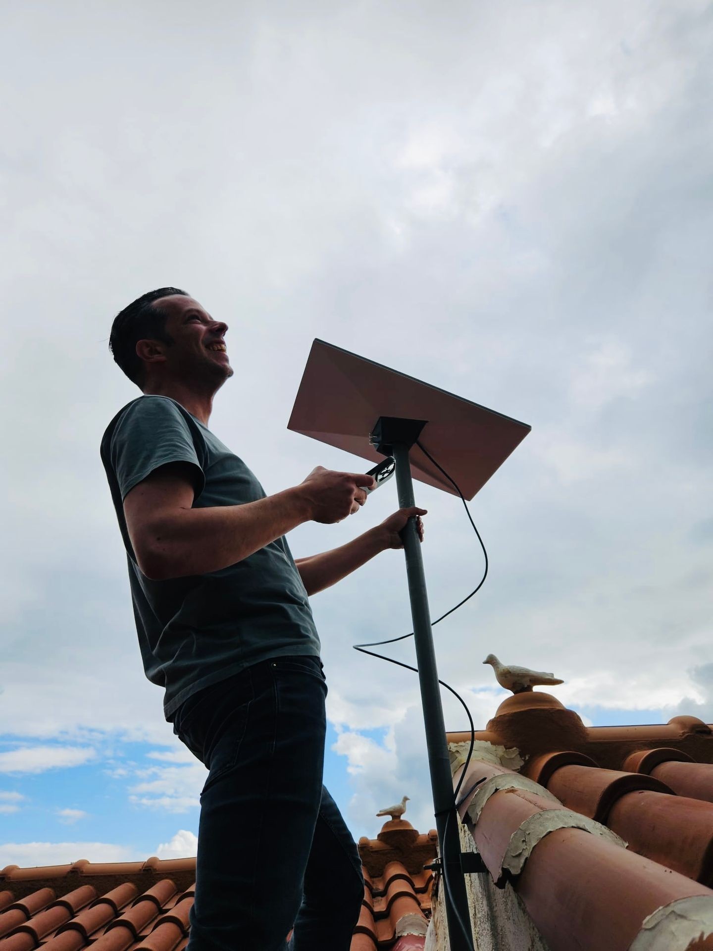 Person on a rooftop adjusting a satellite dish against a cloudy sky background.